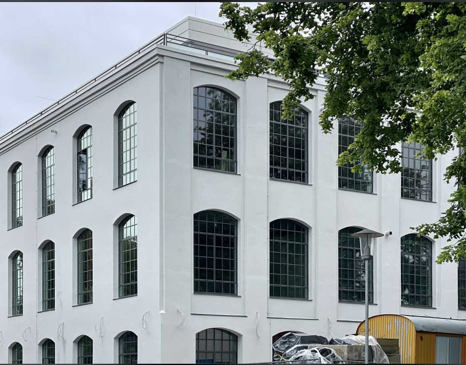 Mehrstöckiges, weißes Gebäude mit großen, rechteckigen Fenstern und Bäumen im Vordergrund.