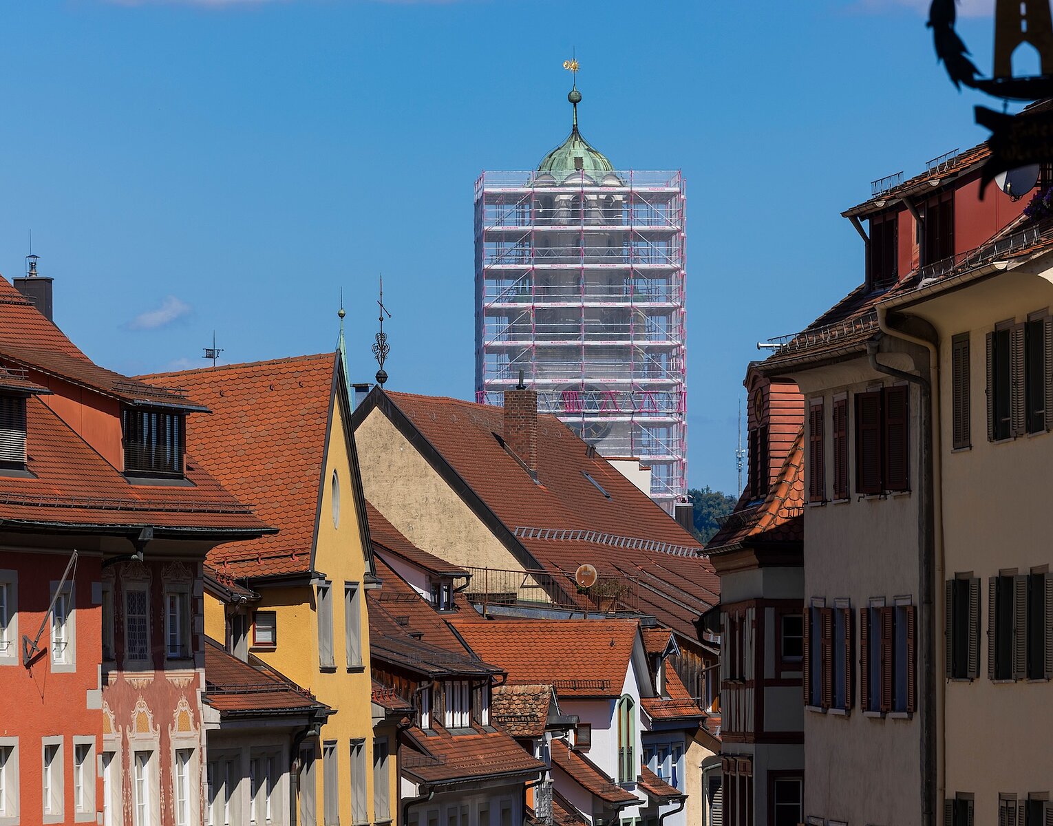 Blick auf eine historische Altstadt mit farbigen Häusern und einem Turm im Hintergrund, der von Gerüsten für Renovierungsarbeiten umgeben ist.