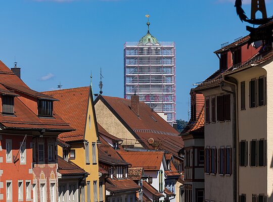 Blick auf eine historische Altstadt mit farbigen Häusern und einem Turm im Hintergrund, der von Gerüsten für Renovierungsarbeiten umgeben ist.