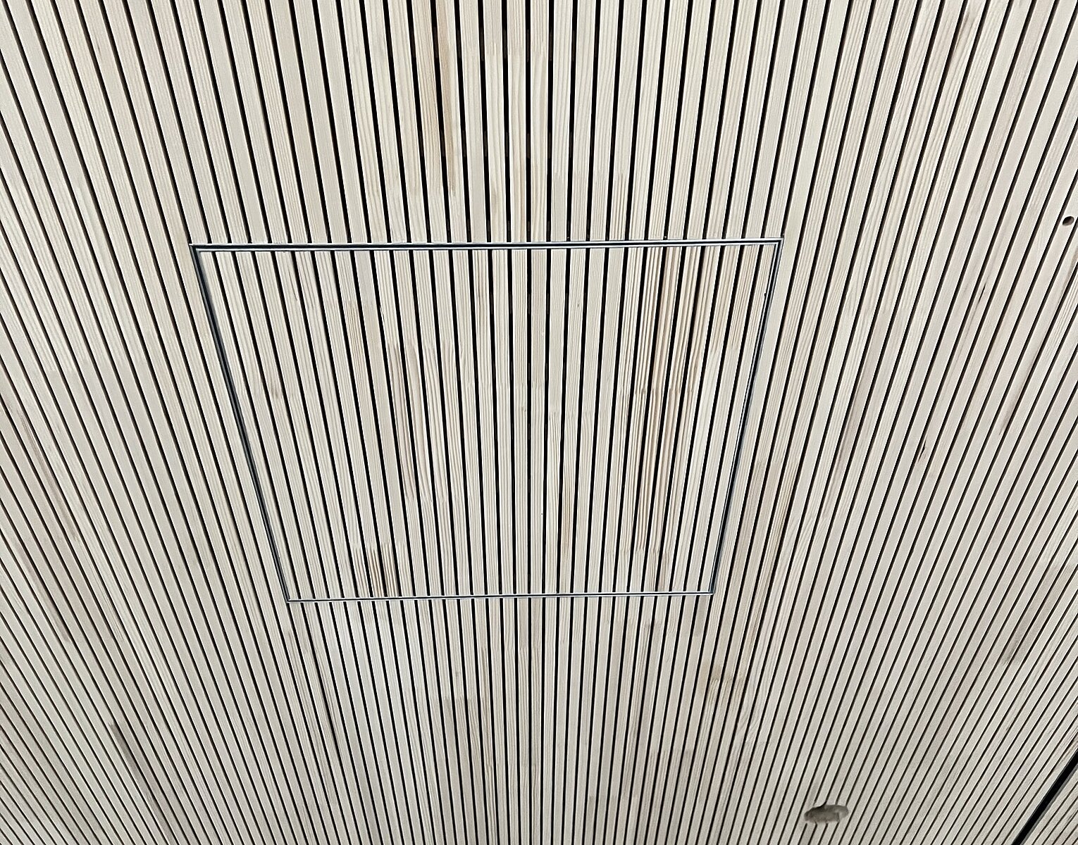 Decke mit vielen parallel verlaufenden schmalen schwarzen Linien auf hellem Hintergrund, darunter eine rechteckige Öffnung.