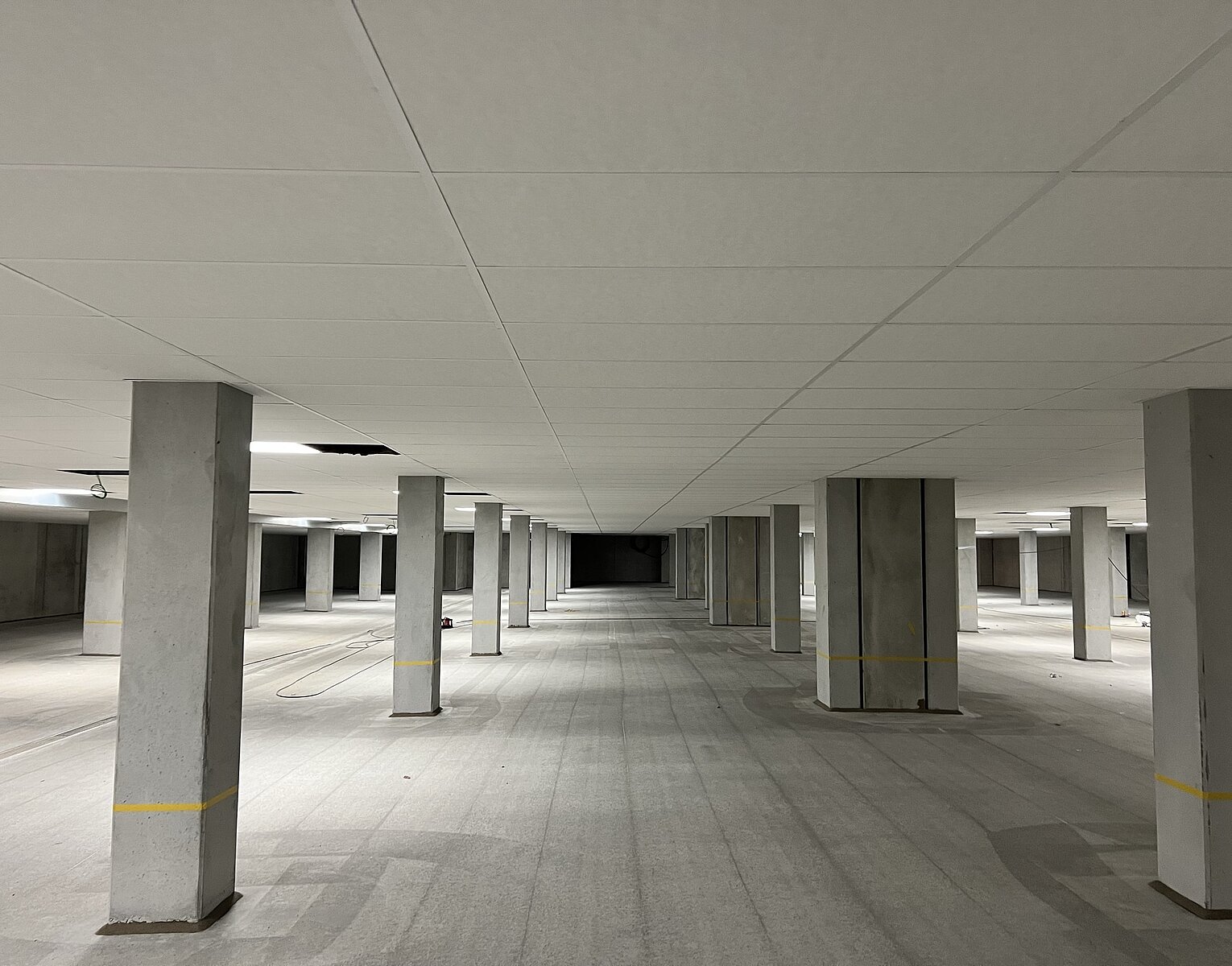 Großer leerer Tiefgaragenraum mit Betonsäulen, glattem Boden und Decke, beleuchtet durch Deckenlampen.