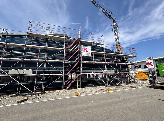 Trockenbau Kaufmann Battle Kart Mehrstöckiges Gebäudegerüst mit Sicherheitsnetzen auf einer Baustelle, Baukran im Hintergrund, klarer Himmel.
