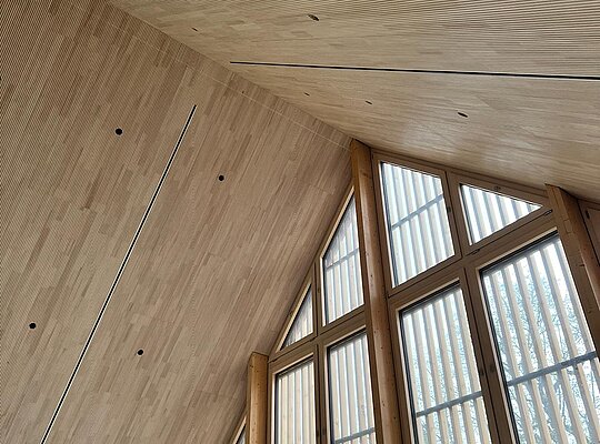Trockenbau Kaufmann Legau Gemeindehaus Innenansicht eines Raums mit hohen, dreieckigen Fenstern und einer holzverkleideten, schrägen Decke.