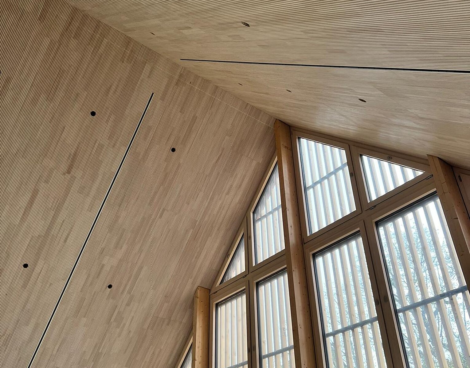 Innenansicht eines Raums mit hohen, dreieckigen Fenstern und einer holzverkleideten, schrägen Decke.
