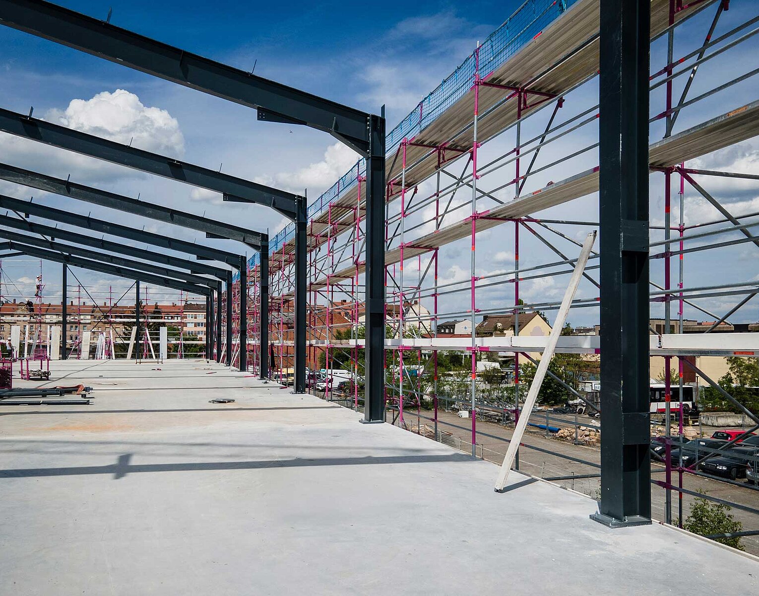 Baustelle eines großen Stahlrahmengebäudes mit Gerüst an der Außenseite und blauem Himmel im Hintergrund.