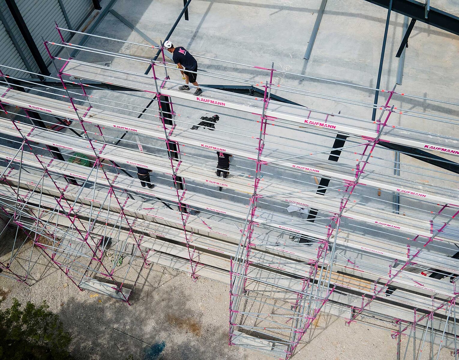Bauarbeiter auf einem Gerüst vor einer großen Gebäudewand aus Betonplatten, die montiert wird.