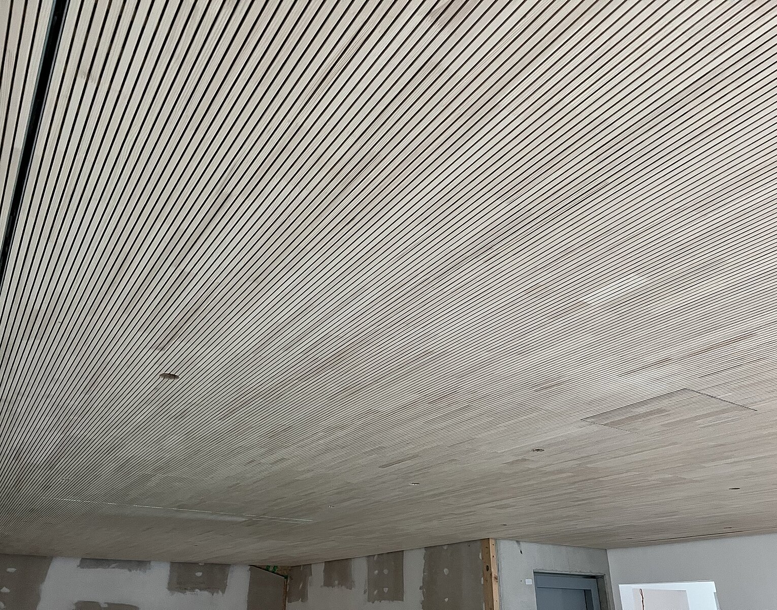 Innenraum eines Gebäudes mit einer Decke aus eng aneinander gereihten Holzlatten und teilweise verputzten Wänden, die sich noch im Bau oder Renovierungszustand befinden.
