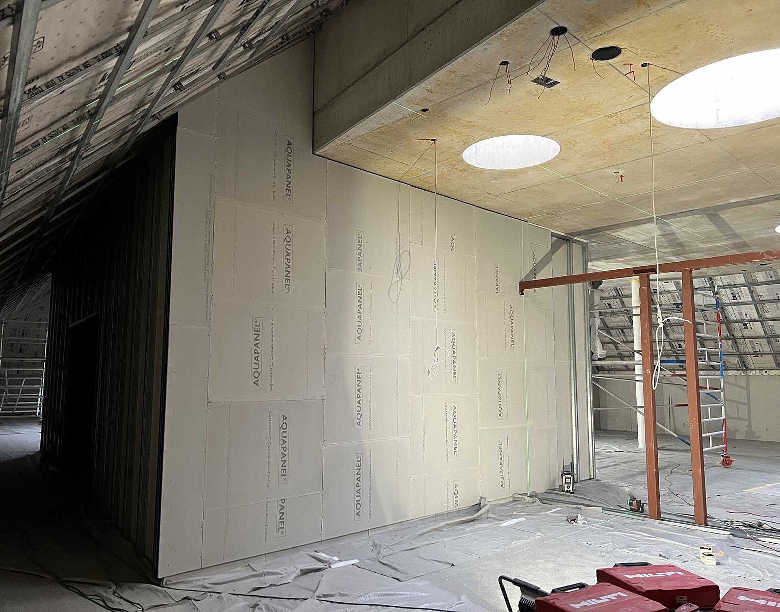 Innenansicht eines Rohbaus mit Trockenbauwänden, freiliegender Decke mit runden Lichtöffnungen und Gerüstgerüst für Bauarbeiten.