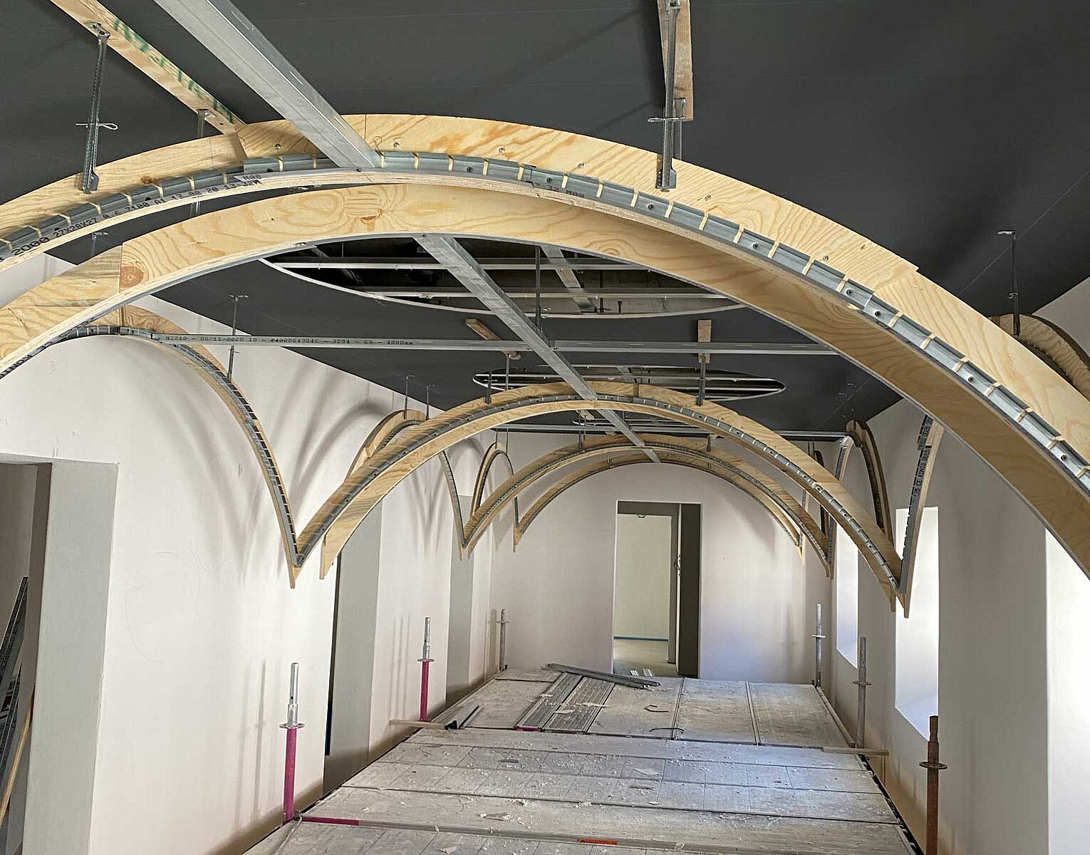 Innenraum eines Gebäudes im Rohbau mit sichtbaren Holzbögen an der Decke und unvollendeten Wänden and Fußboden.