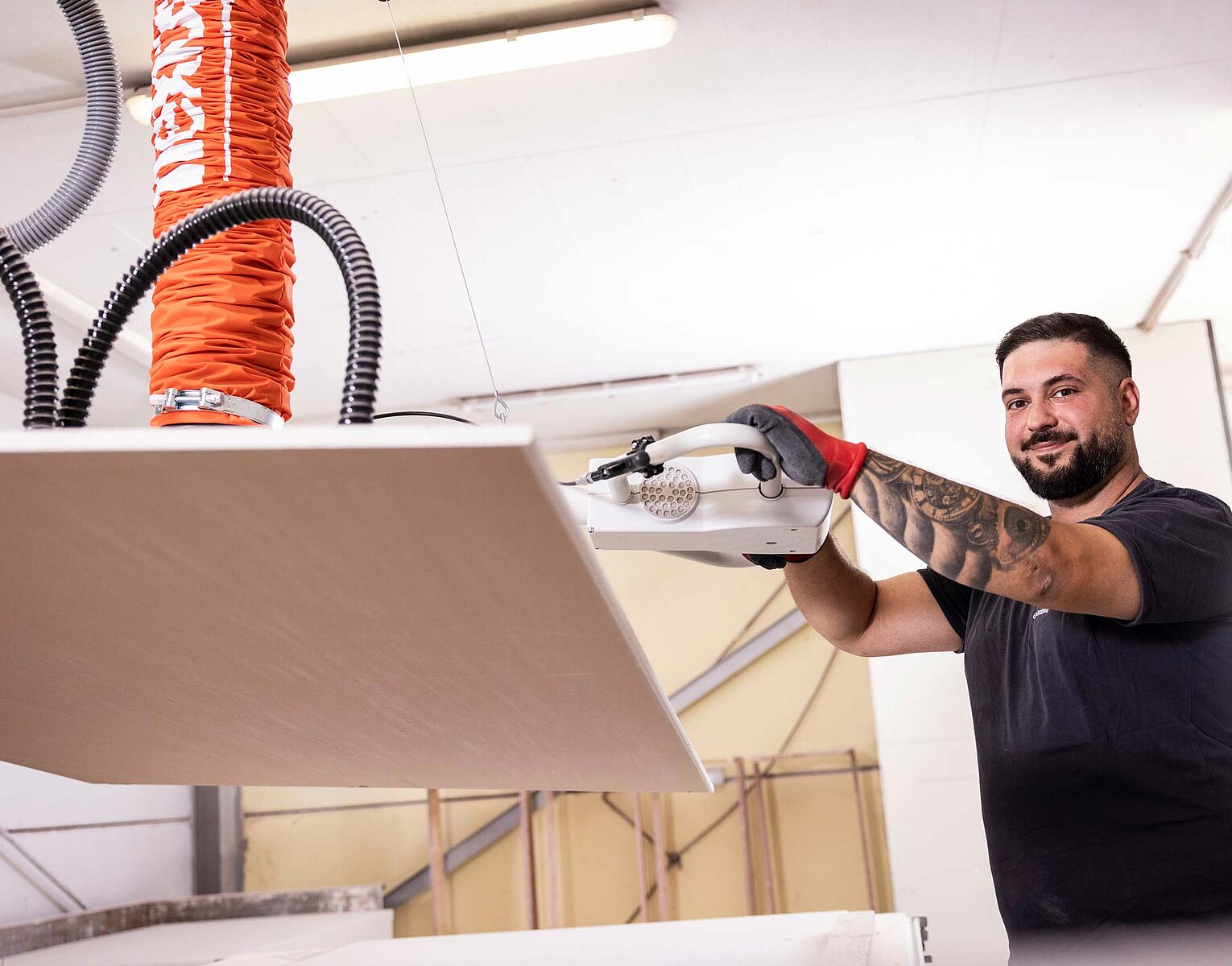 Gerüstbau Kaufmann Ein Mann mit Tattoos und Handschuhen bedient in einer Werkstatt eine Hebemaschine, die eine große Platte anhebt.